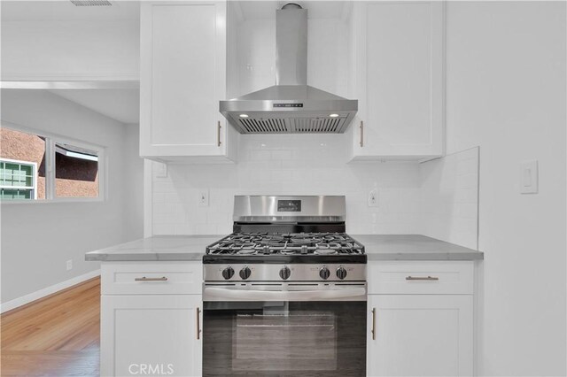 kitchen with baseboards, light stone counters, wall chimney range hood, white cabinets, and stainless steel range with gas cooktop