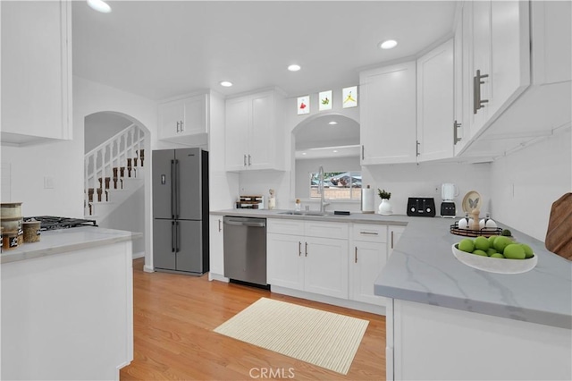 kitchen with light wood-style floors, stainless steel dishwasher, freestanding refrigerator, arched walkways, and white cabinets