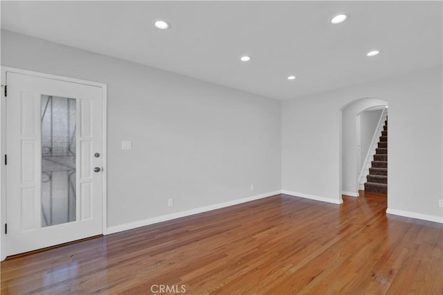unfurnished room with arched walkways, recessed lighting, wood finished floors, stairs, and baseboards