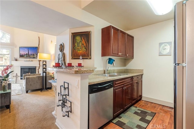 kitchen with open floor plan, stainless steel appliances, a lit fireplace, a sink, and a peninsula