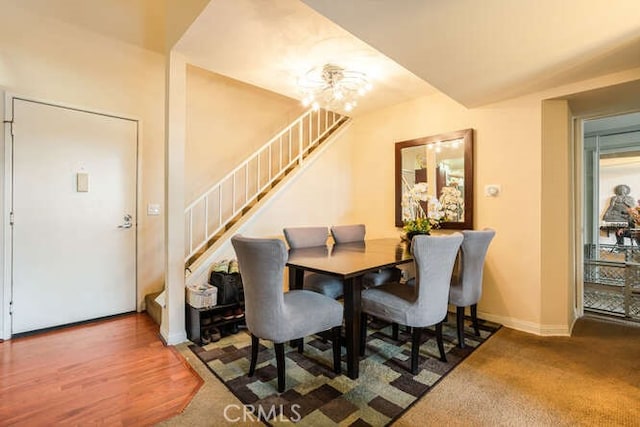 carpeted dining area featuring a chandelier, baseboards, and stairs