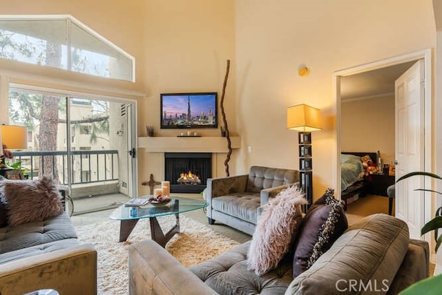 carpeted living area with a warm lit fireplace and a towering ceiling