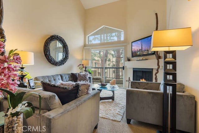 carpeted living room featuring a warm lit fireplace and high vaulted ceiling