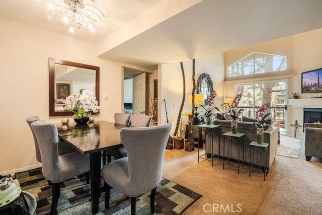 dining area featuring a lit fireplace, carpet, and a notable chandelier