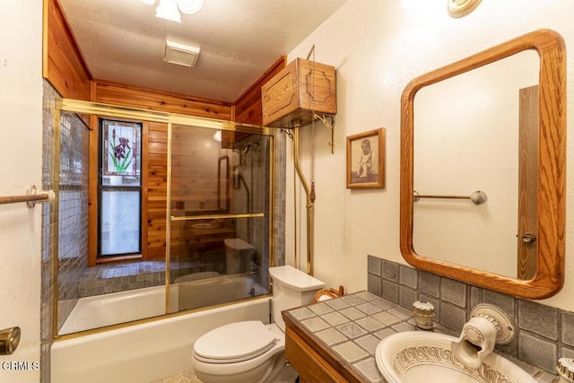 bathroom with toilet, vanity, a textured ceiling, decorative backsplash, and shower / bath combination with glass door