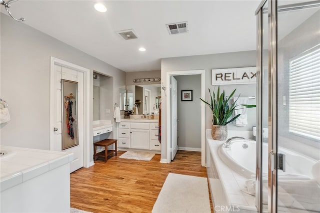 full bathroom featuring vanity, recessed lighting, visible vents, a garden tub, and wood finished floors