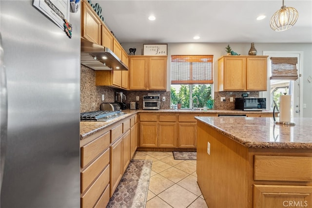 kitchen featuring light tile patterned floors, a sink, under cabinet range hood, stainless steel appliances, and backsplash