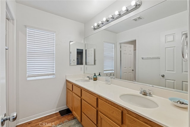 full bath featuring a sink, visible vents, double vanity, and wood finished floors