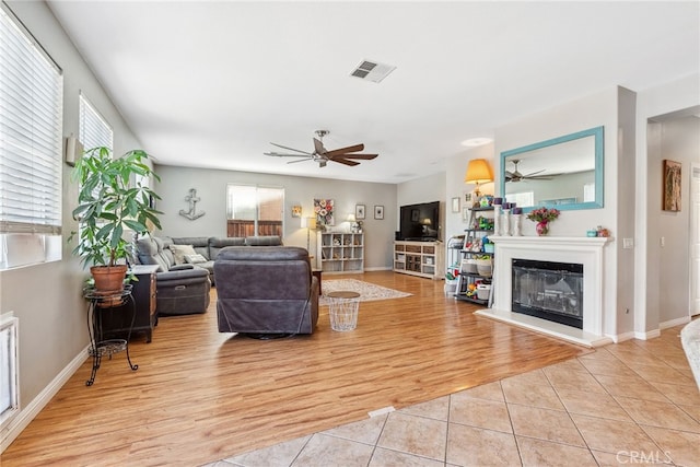 living area with a ceiling fan, visible vents, a glass covered fireplace, light tile patterned flooring, and baseboards