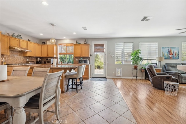 kitchen featuring light tile patterned floors, visible vents, open floor plan, baseboards, and backsplash