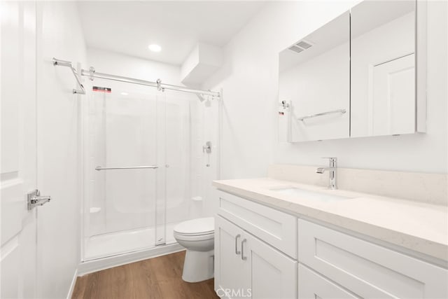 bathroom with visible vents, toilet, a stall shower, and wood finished floors