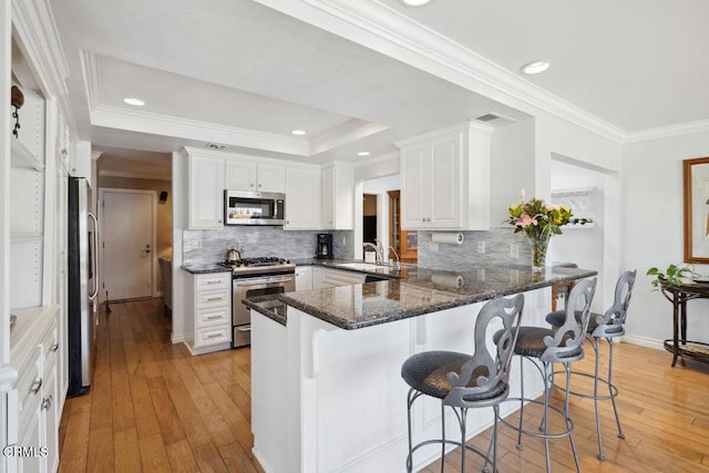2231 Peninsula Rd, Oxnard, CA 93035 - kitchen with appliances with stainless steel finishes, a peninsula, light wood-style flooring, a breakfast bar area, and crown molding