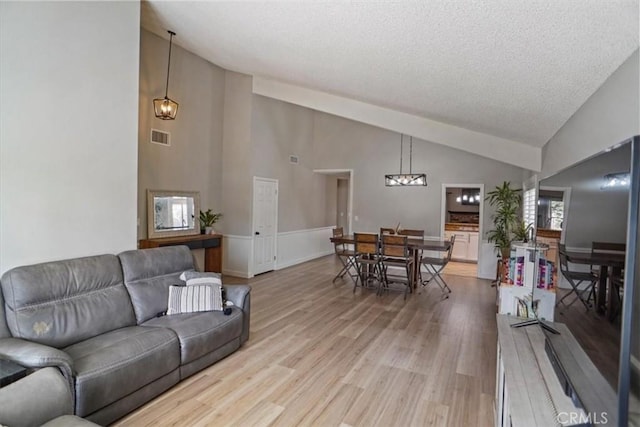 living area with high vaulted ceiling, light wood finished floors, a textured ceiling, and a wainscoted wall