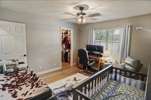 bedroom with light wood-style floors, a walk in closet, a desk, a closet, and a textured ceiling