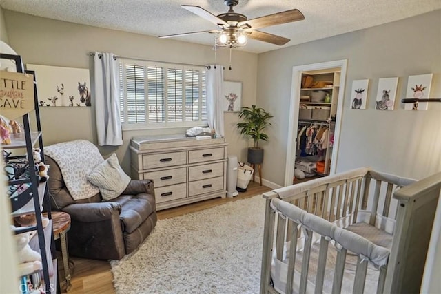 bedroom with light wood-style floors, a textured ceiling, a closet, a spacious closet, and a ceiling fan
