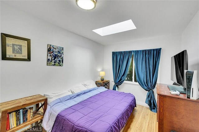 bedroom with wood finished floors, a skylight, and baseboards