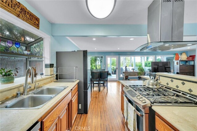 kitchen with brown cabinets, stainless steel appliances, island range hood, a sink, and light wood-style floors