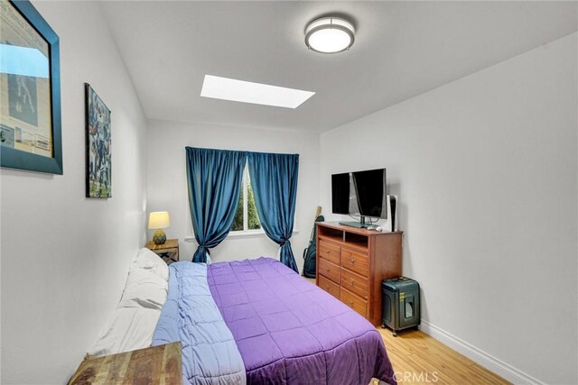 bedroom featuring wood finished floors, a skylight, and baseboards