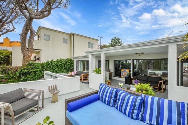 rear view of house with ceiling fan, outdoor lounge area, a patio area, and stucco siding