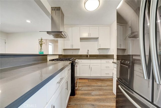kitchen featuring a sink, wall chimney range hood, white cabinets, black range with gas stovetop, and wood finished floors