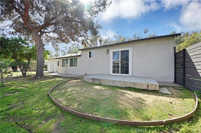 back of house with stucco siding, fence, a patio, and a yard