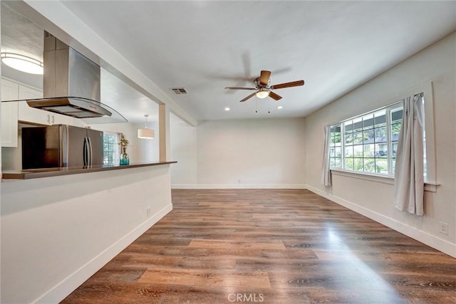unfurnished living room with a ceiling fan, visible vents, baseboards, and wood finished floors