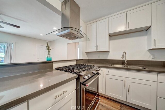 kitchen featuring island range hood, stainless steel stove, a sink, ceiling fan, and white cabinets