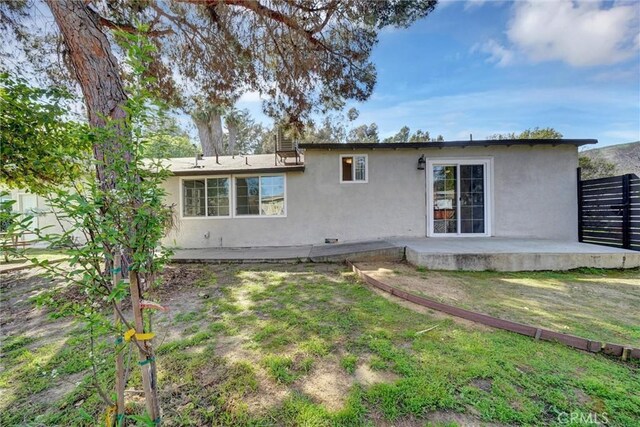 rear view of property featuring stucco siding, fence, a lawn, and a patio area