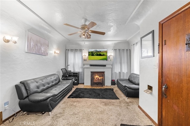 living room with a lit fireplace, carpet, a textured ceiling, ceiling fan, and a textured wall