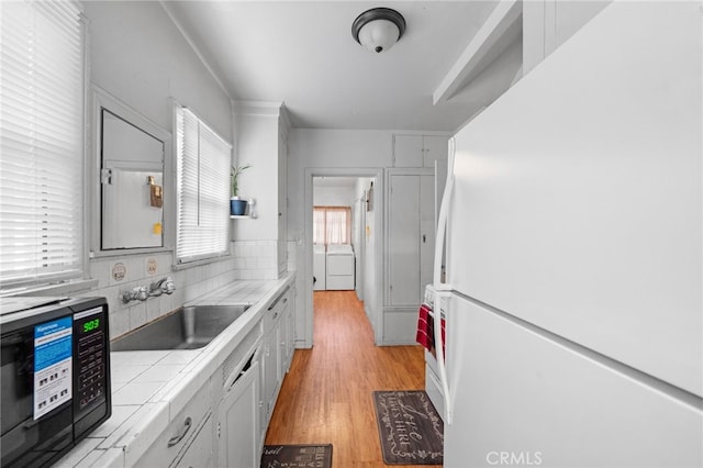 kitchen with tile counters, washer / clothes dryer, a sink, light wood-style floors, and freestanding refrigerator