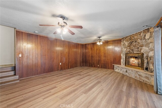 unfurnished living room with wood finished floors, wood walls, a fireplace, and ceiling fan