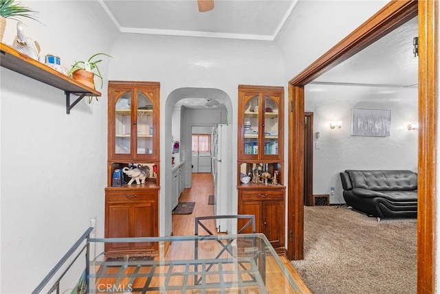 hall featuring carpet flooring, arched walkways, crown molding, and wood finished floors
