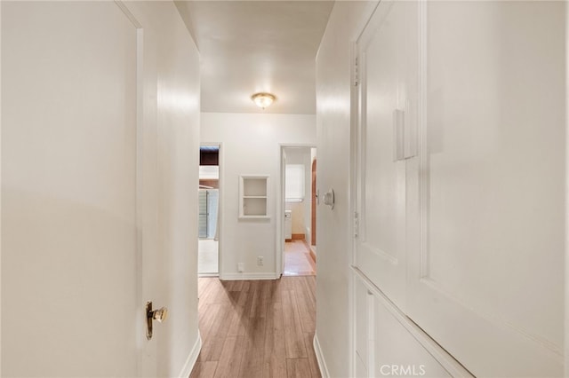 corridor featuring light wood-style flooring and baseboards