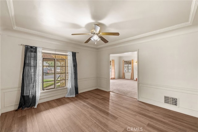 spare room with wood finished floors, crown molding, visible vents, a ceiling fan, and wainscoting