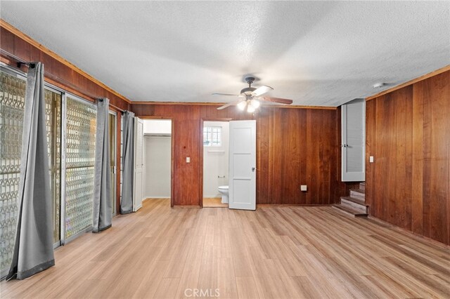 unfurnished bedroom featuring wooden walls, a textured ceiling, ensuite bathroom, light wood-style floors, and ceiling fan