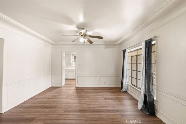 spare room featuring crown molding, a wainscoted wall, wood finished floors, and a ceiling fan