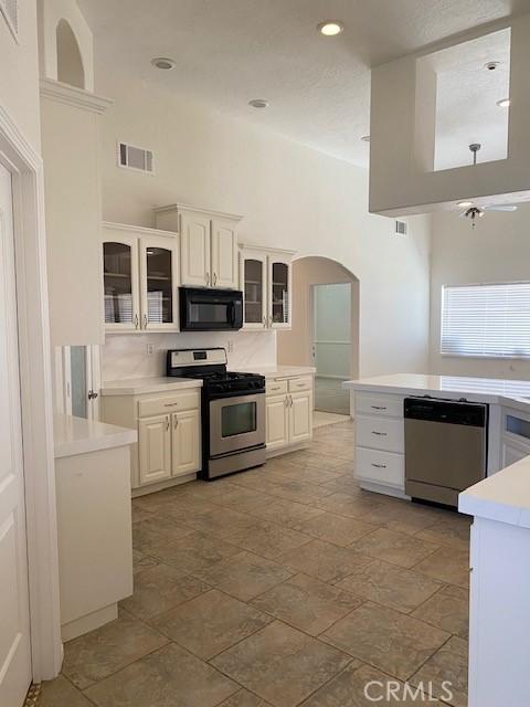 23073 Cielito Dr, Apple Valley, CA 92308 - kitchen with stainless steel appliances, light countertops, arched walkways, glass insert cabinets, and a high ceiling