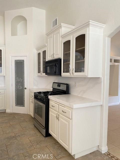 23073 Cielito Dr, Apple Valley, CA 92308 - kitchen with black microwave, gas range, light countertops, glass insert cabinets, and white cabinetry