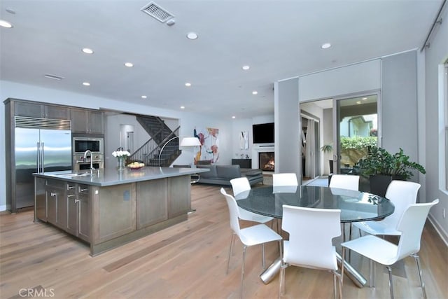 14608 Mccormick St, Sherman Oaks, CA 91411 - kitchen with built in appliances, a sink, a warm lit fireplace, a center island with sink, and light wood-style flooring