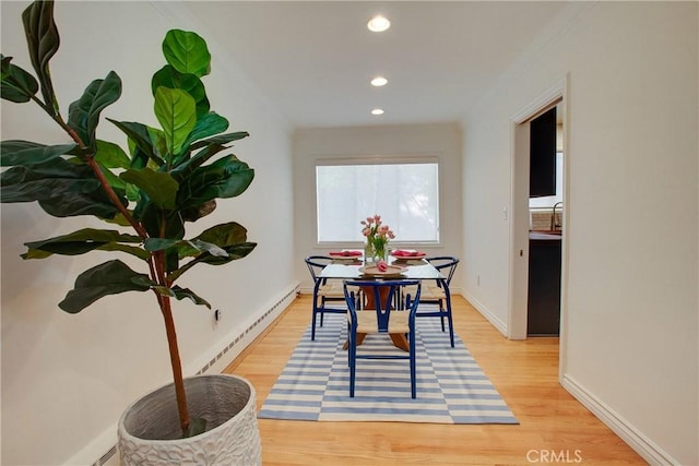 dining area with a baseboard radiator, light wood-style floors, and ornamental molding