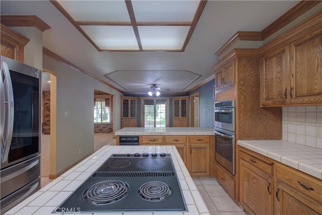 kitchen with ornamental molding, stainless steel appliances, backsplash, tile countertops, and brown cabinets