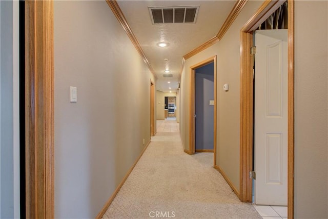 hallway with light colored carpet, visible vents, crown molding, and baseboards
