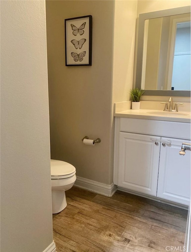 half bath featuring baseboards, toilet, vanity, and wood finished floors
