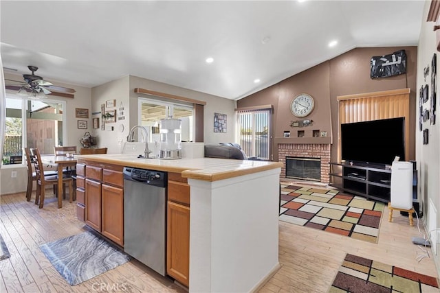 kitchen featuring tile countertops, a sink, open floor plan, vaulted ceiling, and stainless steel dishwasher