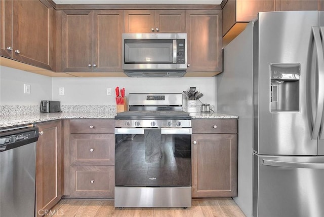 kitchen featuring light wood-style floors, appliances with stainless steel finishes, and light stone counters