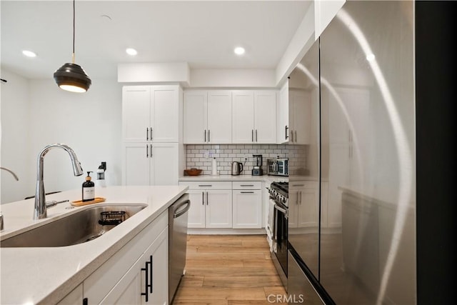 kitchen featuring light countertops, white cabinetry, a sink, light wood-style flooring, and appliances with stainless steel finishes
