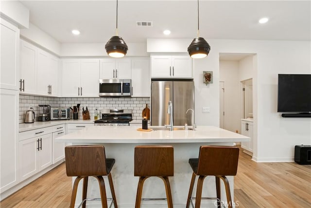 kitchen with appliances with stainless steel finishes, tasteful backsplash, light wood-type flooring, visible vents, and a kitchen bar