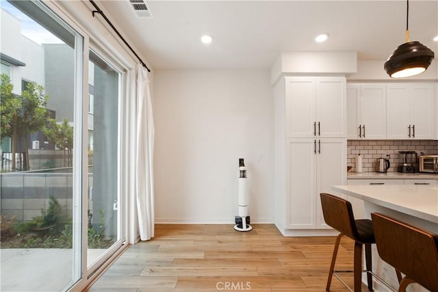 kitchen with light countertops, white cabinetry, light wood-type flooring, backsplash, and visible vents