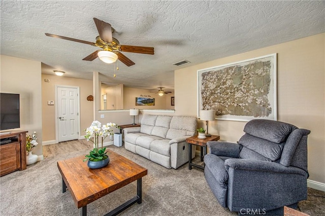 living room featuring a textured ceiling, baseboards, a ceiling fan, and visible vents