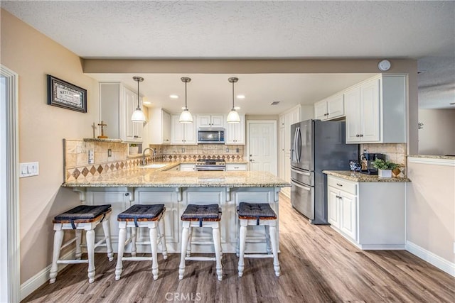 kitchen featuring light stone countertops, light wood-style flooring, a peninsula, appliances with stainless steel finishes, and a sink